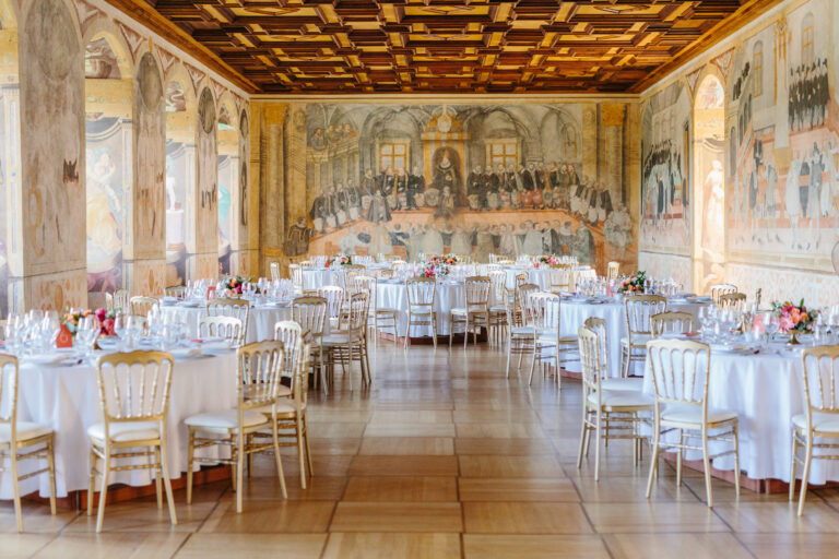 Banquet hall with frescoed murals on walls, ornate ceiling, and round tables set for a formal dinner.