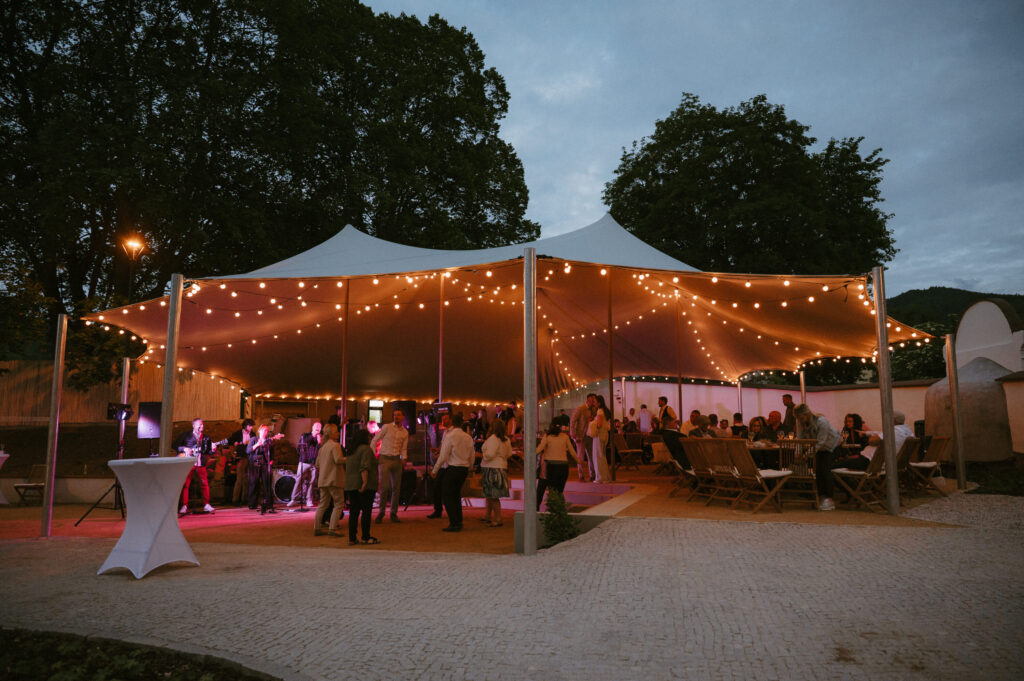 Outdoor evening event under a large white tent with string lights and guests mingling.